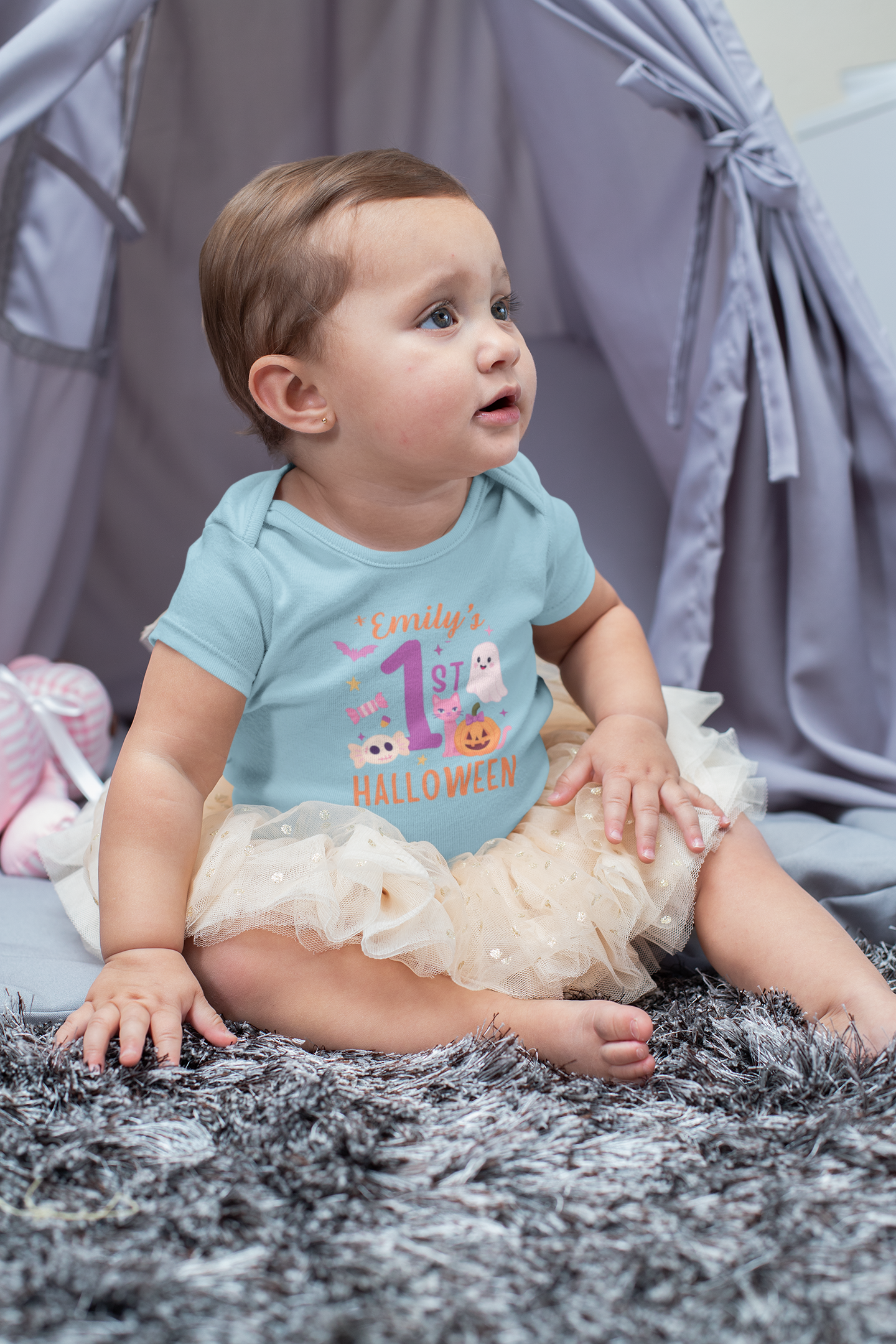Baby wearing a light blue Halloween-themed onesie sitting on a gray surface.